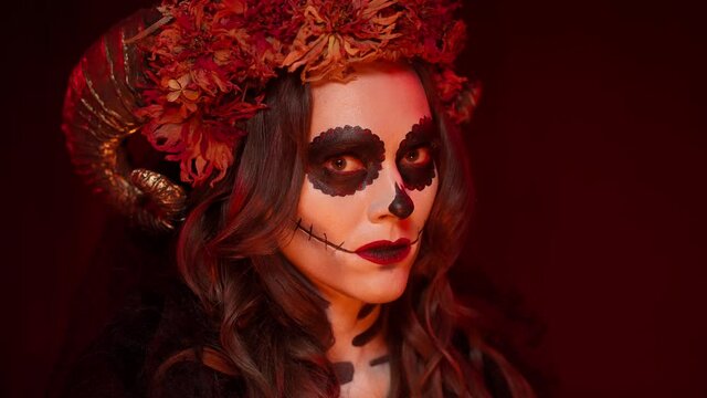 beautiful, chewy Halloween makeup for catrina-style women of the Spanish Day of the Dead with ram horns, flowers, dark eyes, red lips. Large portrait in a fiery room