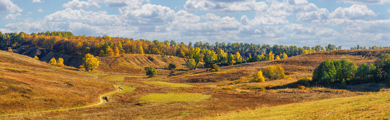 Naklejka premium Autumn landscape, panorama, background - view of the valley with dirt rural road surrounded by wooded hills, horizontal banner