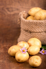 Raw potatoes with flowers in the bag on the wooden background