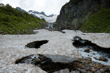 mountain landscape, melting snow, glacier and mountain stream, caves in ice