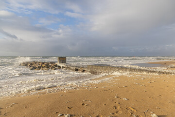 Major storm at the beach with huge crashing wave on a wooden and rocky  groyne (breakwater) with ecume under a stormy sky