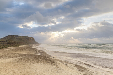 A scenic view of a beach along cliff with huge waves and foam under a stormy sky and ray of light