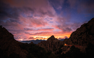 Fototapeta na wymiar Sunrise over the Calanches of Piana in Corsica with lightning in the distance and car lights passing along the D81 road
