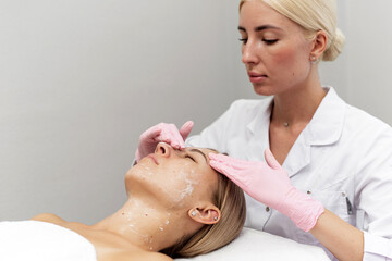 Obraz na płótnie Canvas Woman beautician cleans and moisturizes patient's skin in spa salon