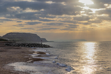 A scenic view of a beautiful sunrise at the beach with some hill in the background and marble sky