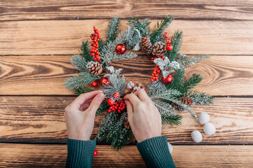 Girl decorates a Christmas wreath on a wooden table