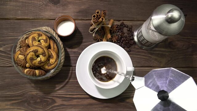 The process of brewing instant coffee.On a wooden table, a cup with coffee, cookies and a milk jug.