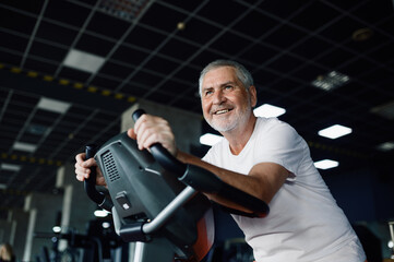Fototapeta na wymiar Elderly man poses on exercise bike in gym