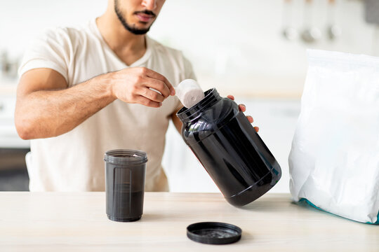 Unrecognizable young sporty guy making protein shake at table in kitchen, closeup