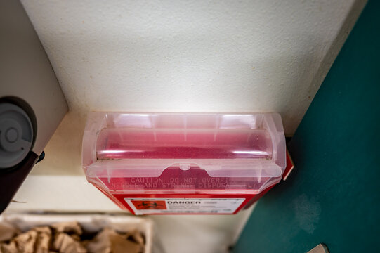 Red biohazard sharps waste container mounted to the wall of a public restroom