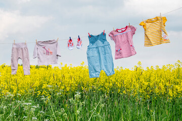 Eine Wäscheleine mit Kinderkleidung hängt an einem gelben Rapsfeld