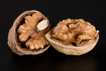 Two split beautiful textured walnuts in a shell on a glossy black background with reflection