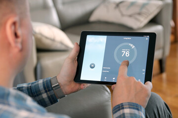 Man is Adjusting a  temperature using a tablet with smart home app in modern living room