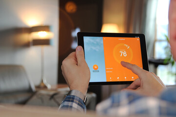 Man is Adjusting a  temperature using a tablet with smart home app in modern living room