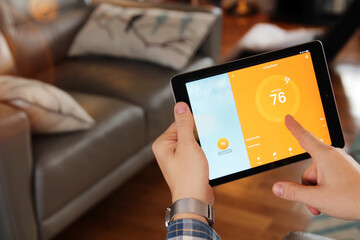 Man is Adjusting a  temperature using a tablet with smart home app in modern living room.