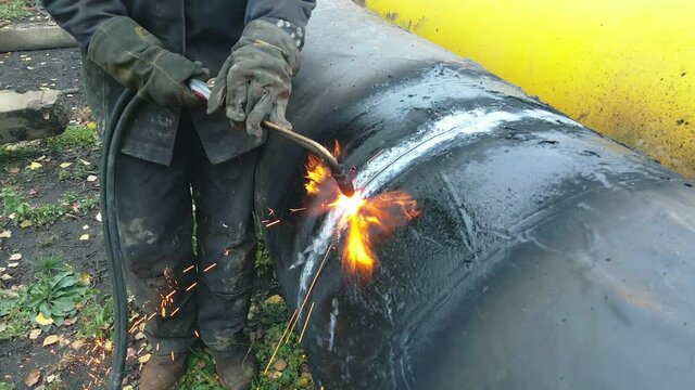 The welder cuts a large pipe with acetylene welding for gasification. Disposal of old used metal pipes. Authentic workflow scene. Industrial background.