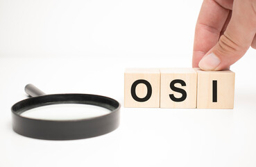 osi text wooden cube blocks and hand holding magnifying glass on table background. - obrazy, fototapety, plakaty