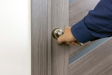 The man's hand opens the gray classic door behind the doorknob.