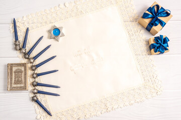 Jewish holiday Hanukkah concept with white napkin, menorah, Torah and gift box over white wooden background