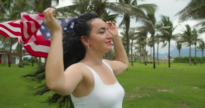 Patriotism, independence day and holidays concept - happy smiling young woman in swimsuit with national american flag on summer beach.
