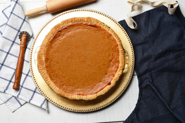 Fresh baked homemade pumpkin pie on a white wood table with apron, rolling pin and crimper.
