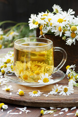 Camomile herbal tea in a glass cup with blossoms on wooden rustic background, closeup, herbal beverage is good for sleep, skin and hair care, natural medicine and naturopathy concept