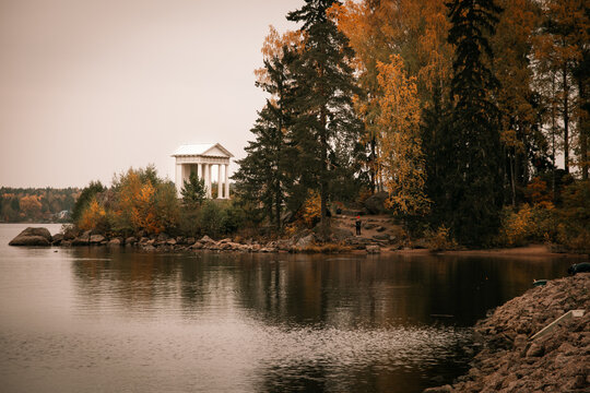 the pond is dark in color. there is a white granite gazebo on the shore of the lake. a white gazebo among the trees. trees with yellow and orange leaves. autumn landscape on the lake