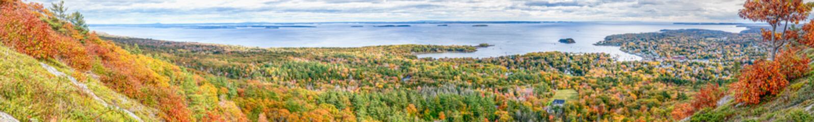 Autumn foliage covers the landscape around Penobscot Bay and the village of Camden, Maine as seen from atop Mount Battie in Camden Hills State Park in this wide photographic panorama. - 466024704