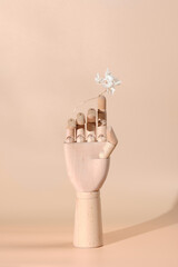 a figurine for decoration a wooden human hand on the finger of which a dried white orchid flower is balancing. Modern monochrome pop-collage in trendy beige colors