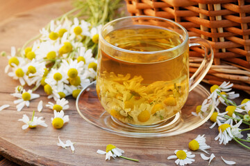 Camomile herbal tea in a glass cup with blossoms on wooden rustic background, closeup, herbal beverage is good for sleep, skin and hair care, natural medicine and naturopathy concept