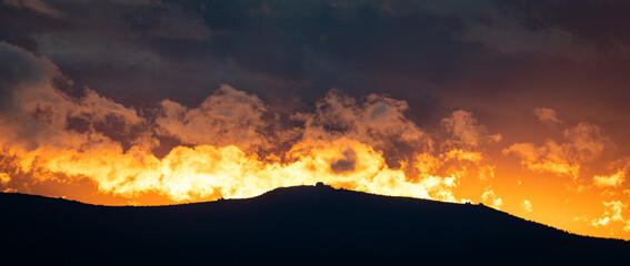 Amazing sunset in the mountains that looks like a fire. Flaming clouds. Red dusk. Evening orange. Dramatic sunset.