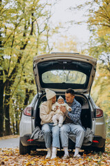 Young family with baby daughter sitting in the back of their car in the autumnal forest