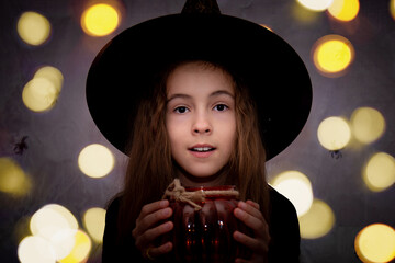 Children's halloween. A smiling girl in a witch hat and an black T-shirt with a glass jar in the...
