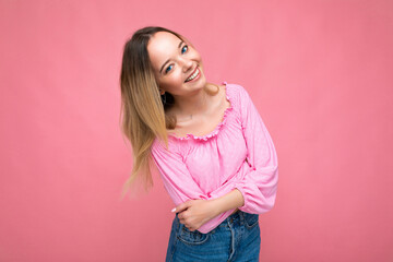 Portrait of young beautiful smiling hipster blonde woman in trendy pink crop top blouse. Sexy carefree female person posing isolated near pink wall in studio. Positive model with natural makeup. Copy
