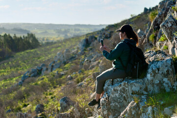 Obraz premium young woman above the mountains in the middle of nature taking photos of the landscape and likewise with a sunny day.