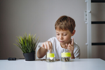 little caucasian boy putting coin into glass bottle at the table. Kid saving money for education