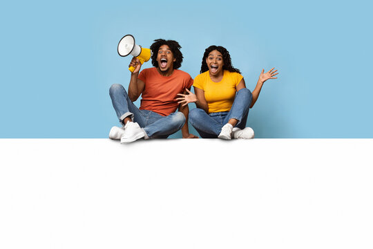 Emotional black couple sitting on empty horizontal board for advertisement