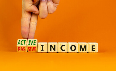 Passive or active income symbol. Businessman turns wooden cubes and changes words passive income to active income. Beautiful orange background, copy space. Business, passive or active income concept.