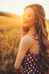 View from the side of a young woman smiling in the wheat field. Freckled face and shoulders. Sunset in the wheat field