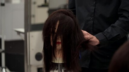 Caucasian guy in black clothes cuts the mannequin's hair