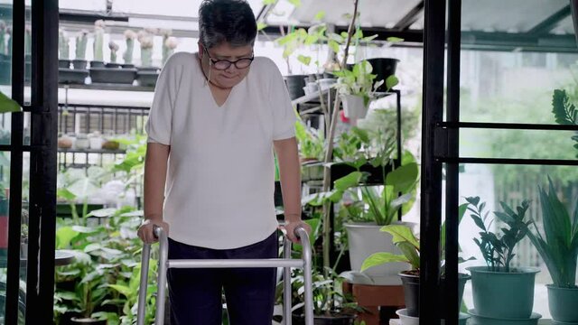 elderly Asian woman uses a walker to walk alone inside her home.
