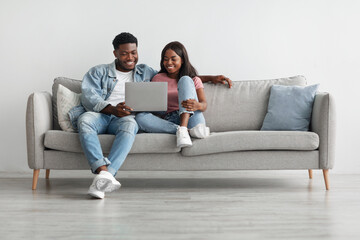African american couple sitting on couch, using laptop