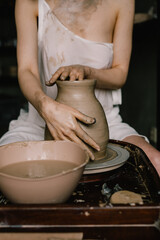 young girl in a white shirt makes a pitcher of clay on a potter's wheel. Pottery workshop of a creative woman. Concept - hobby clay modeling