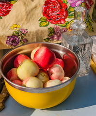 Apples in a yellow metal container and a crystal decanter close-up on the background of a kitchen towel in summer