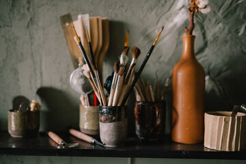 Accessories and items on the shelf in pottery workshop: brushes, glasses, jugs. workshop of master of pottery. concept - clay modeling