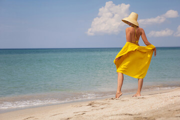 young fashionable woman in a yellow hat dress and sun glasses is posing on beach in summer on...