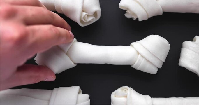 A person putting a Rawhide Dog Chew Bone on a black background table