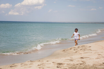 boy child in striped shorts and a white T-shirt walks on sandy beach and in sunglasses