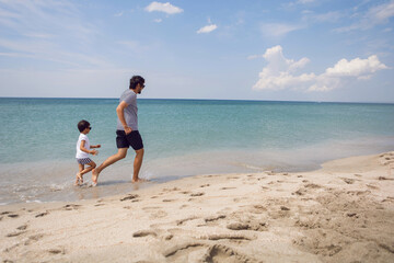 father in a striped T-shirt walks with his son in shorts and a T-shirt walking on beach in summer during a vacation