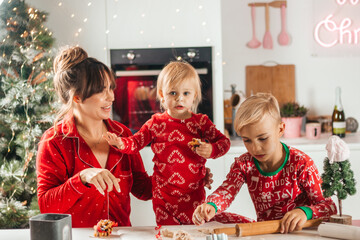 happy family mother, son and daughter in red pajamas bake cookies for christmas
